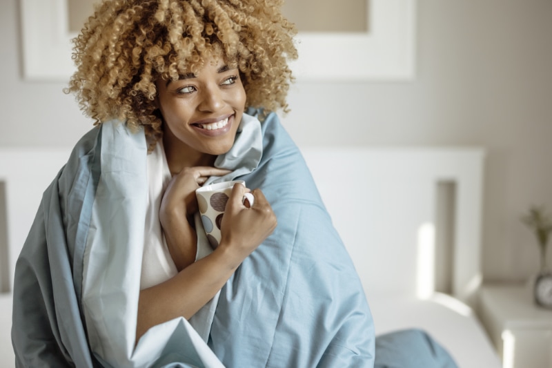 Young woman snuggled up under duvet, happy her gas furnace is finally working.