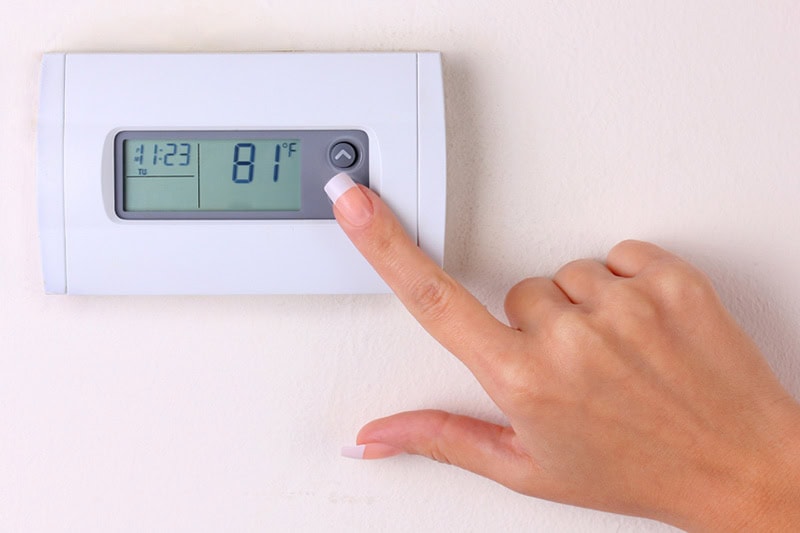 Thermostat 101: Basic Buyer’s Guide. A person changing the temperature in their home.