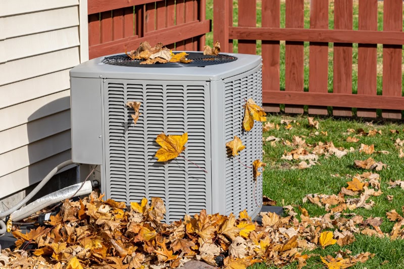 Technician ready to remove leaves around a heating and cooling system as part of the homeowner's fall HVAC maintenance plan.